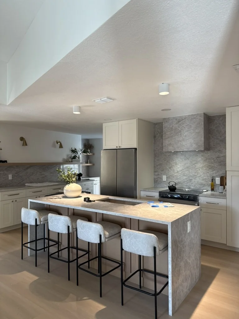 Completed white kitchen with stone-wrapped island and four counter stools